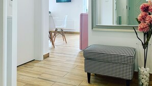 A hallway with a wooden floor, a pink cabinet, a houndstooth ottoman, a large mirror, and a television in the background. - The Apartment is in a calm, quiet location at the Lake Balaton! (Keszthely)