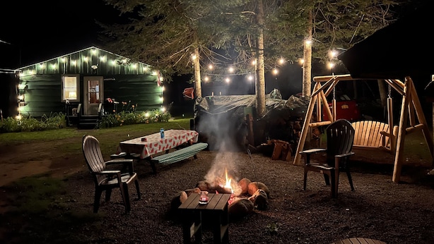 En rustik utomhusmiljö med en eldstad, ett picknickbord och trästolar.