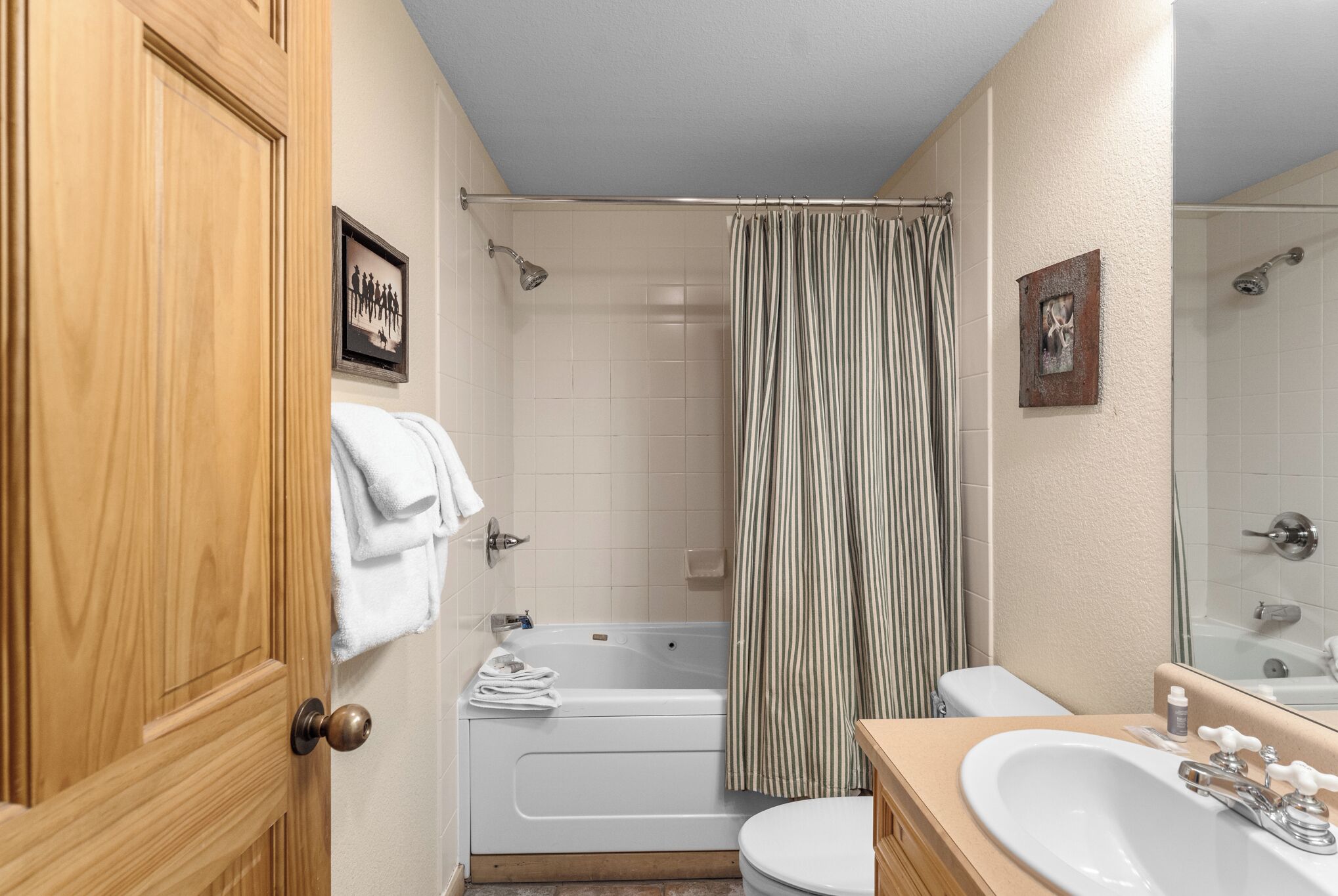 A bathroom with a wooden door, white bathtub, striped shower curtain, and a white sink with a mirror.