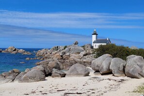 A white lighthouse on a rocky shore with clear blue water.