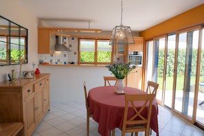 Una cocina moderna con armarios de madera, una mesa de comedor con mantel rojo y un ventanal con vistas a la vegetación.