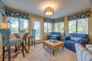 A living room with a glass coffee table, two blue sofas, and patterned chairs.