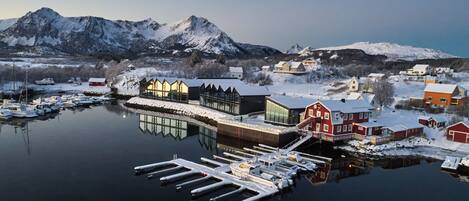 A marina with boats docked, a wooden pier, and buildings with snow-covered roofs.
