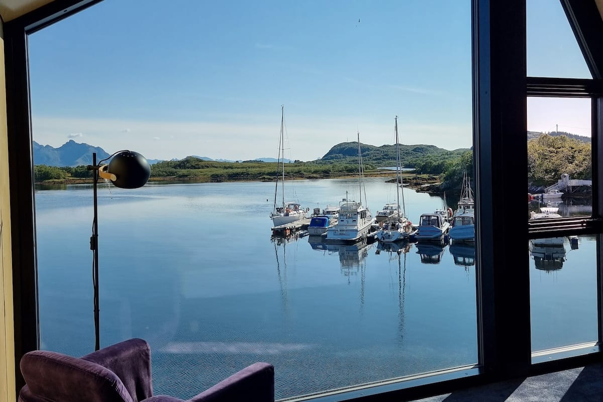 A room with a large window overlooking a marina with boats, a bed, and a chair.