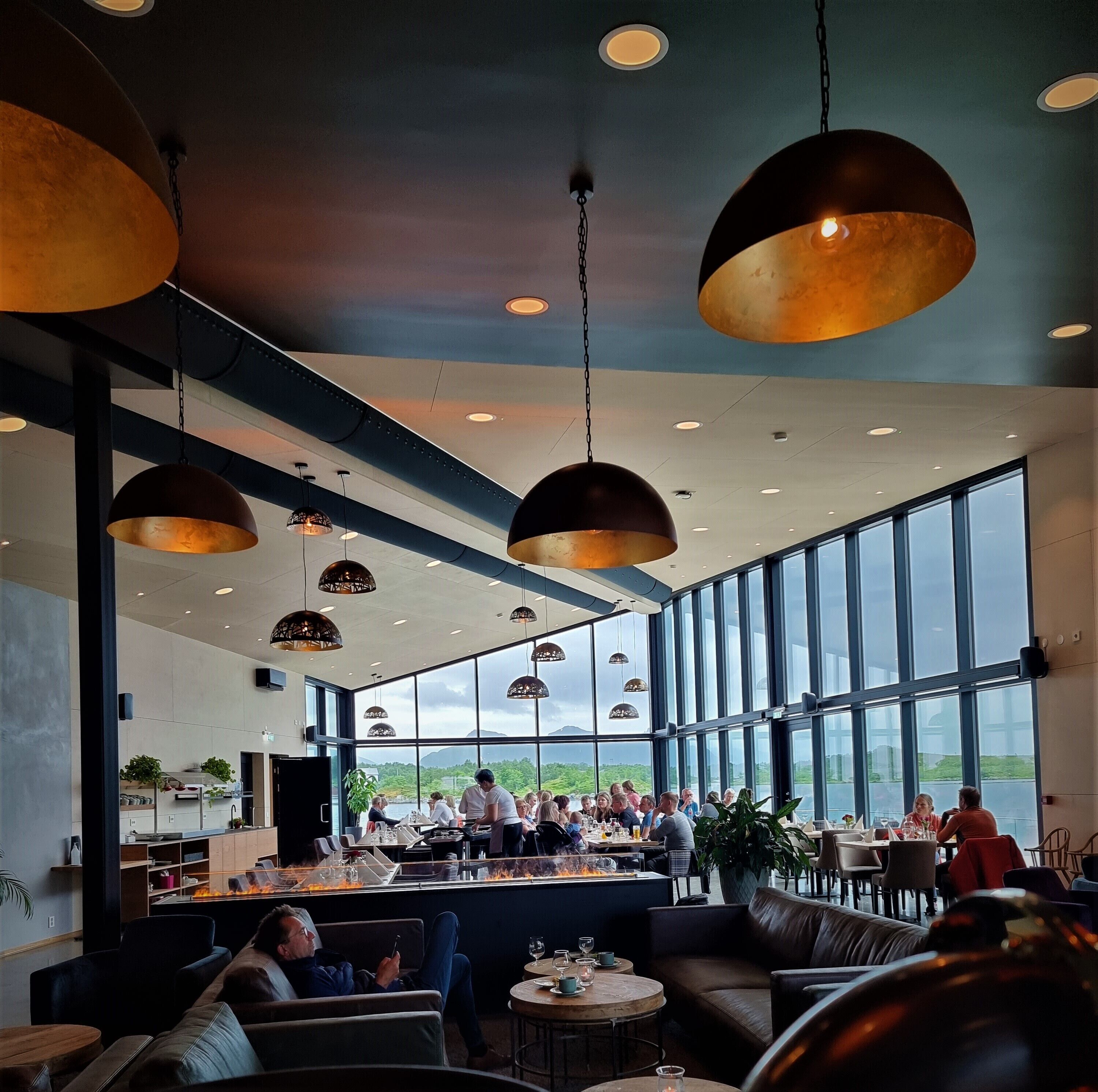 A spacious restaurant with high ceilings, large windows, and hanging pendant lights.