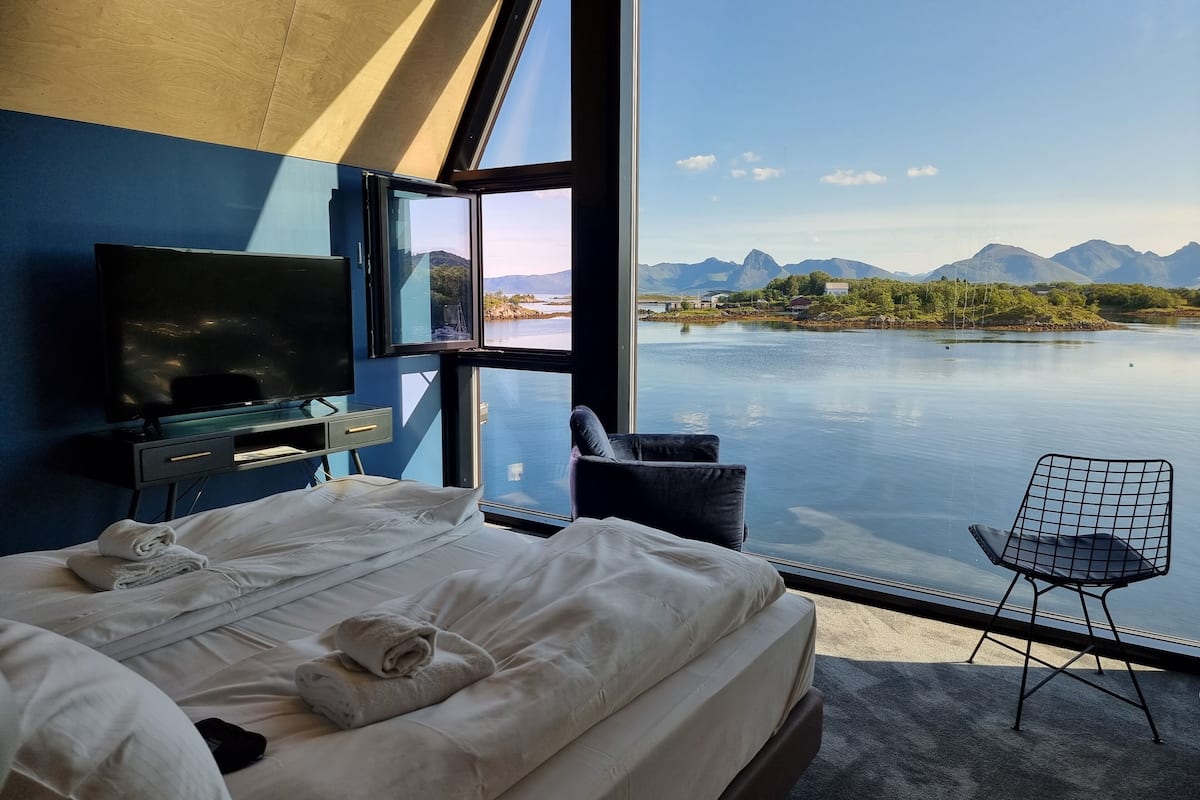 A hotel room with a large bed, a TV, and a view of a lake and mountains.