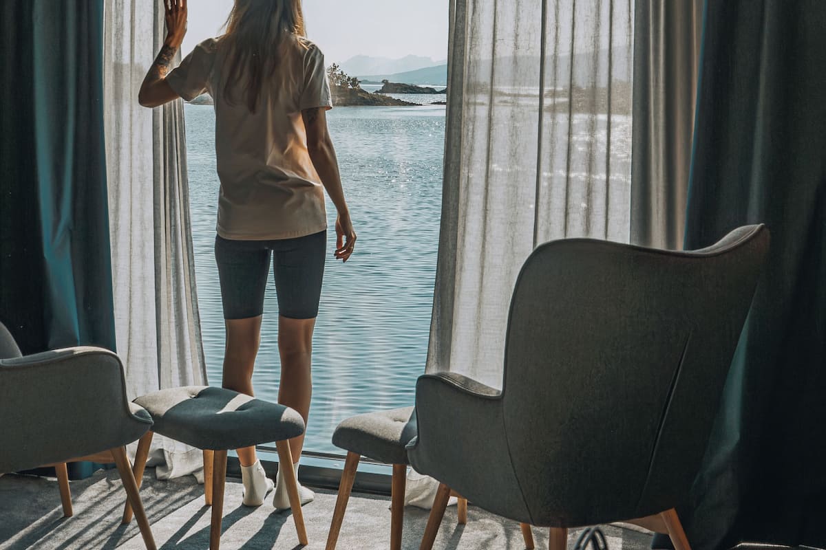 A room with a large window, a view of a body of water, and two chairs.