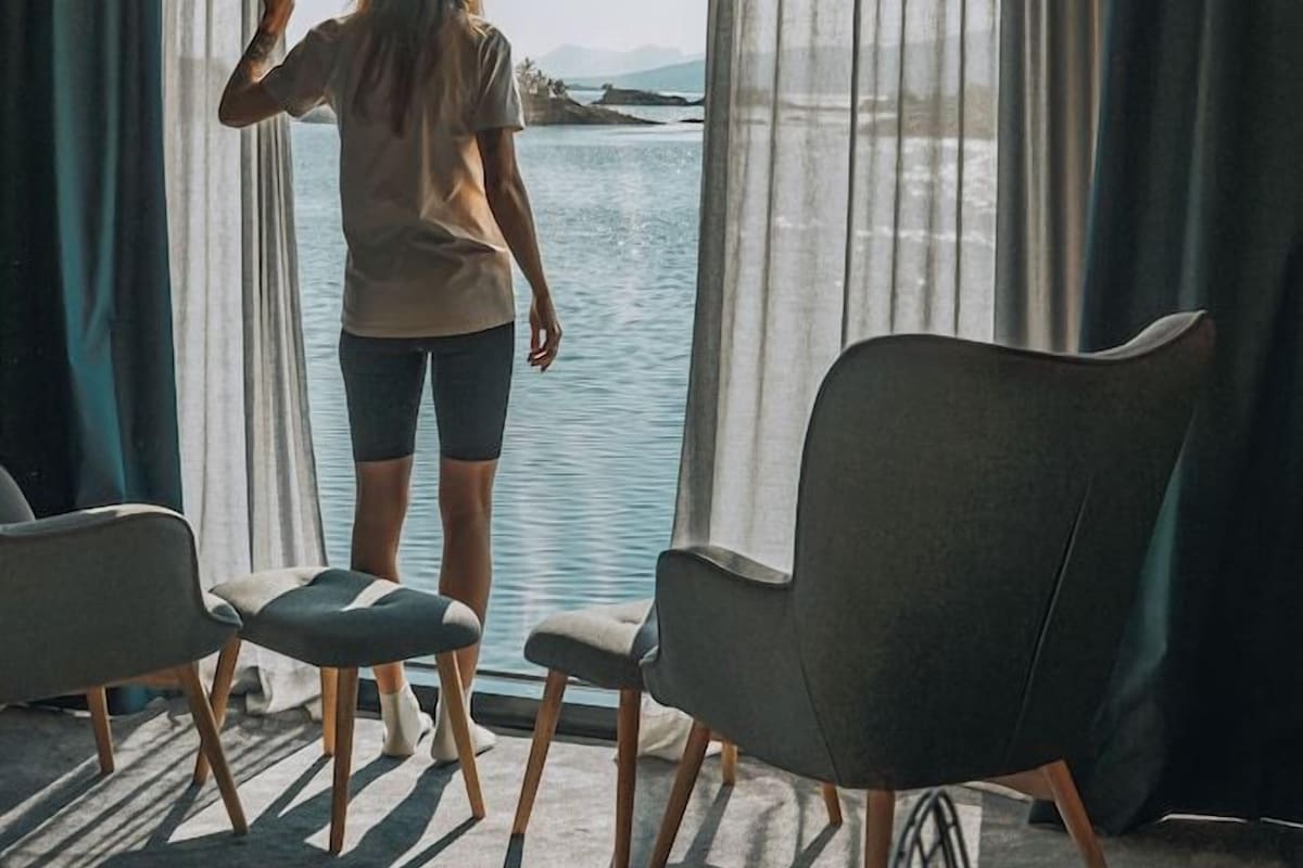 A room with a large window, a person standing by the window, and two chairs.
