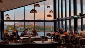 Un restaurante con amplios ventanales que ofrece vistas a un lago y montañas.