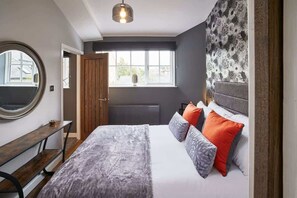 Une chambre à coucher avec un grand lit, un miroir rond, un banc en bois et une fenêtre donnant sur l’extérieur.