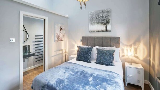 Quarto moderno com cama, mesa de cabeceira, luminária na parede e uma pintura.