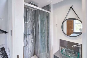 Un bany modern amb dutxa tancada per vidre, un mirall rodó i un lavabo de vidre.