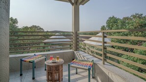A balcony with a view of greenery, a table with a woven chair, and a small round table with drinks and a bowl. - Sterling Gir (Mendarda)