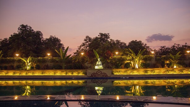 A nighttime pool area with a statue in the center, surrounded by well-lit plants and trees. - Sterling Gir (Mendarda)