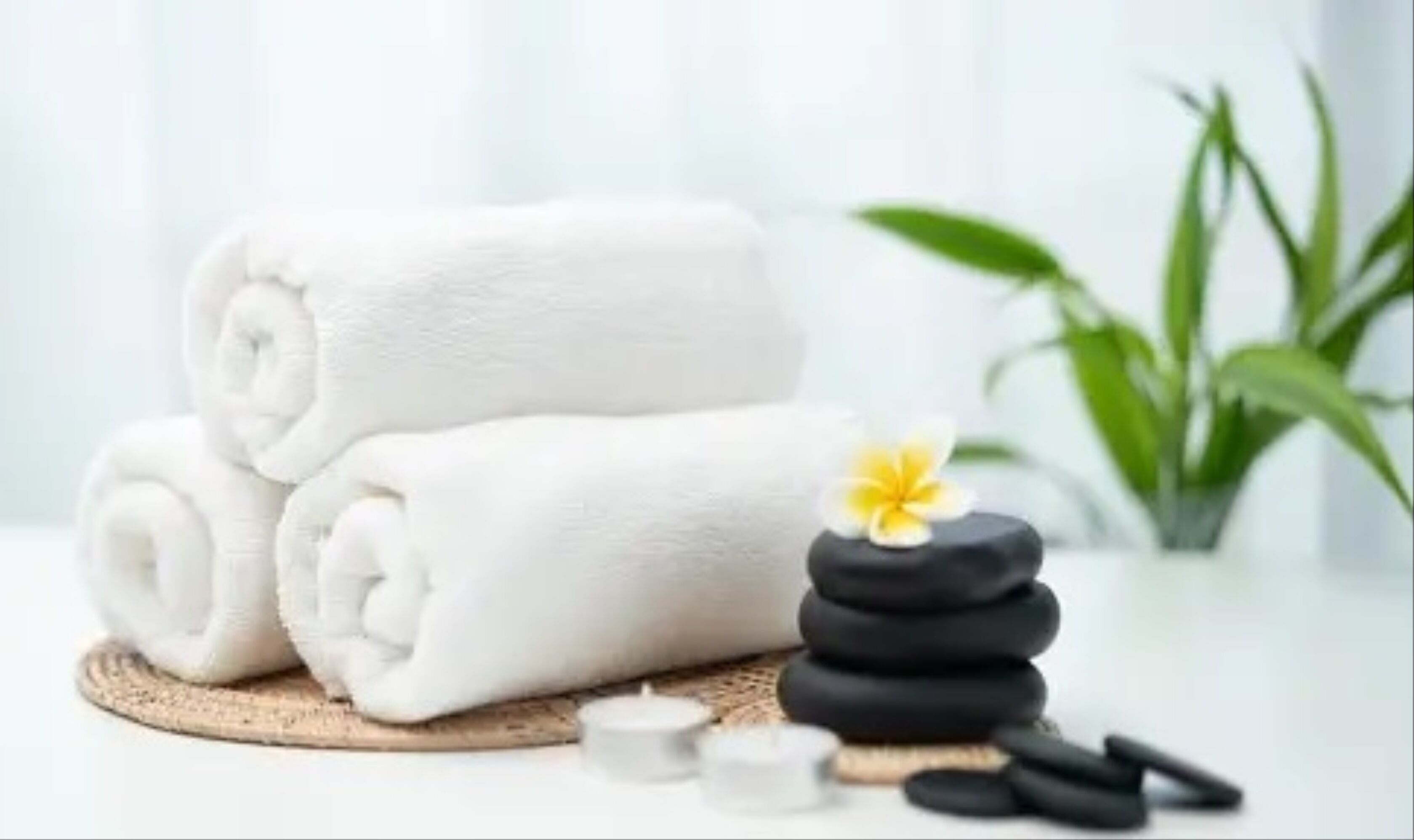 A stack of white towels, a small yellow flower, and a stack of black stones on a wooden surface.