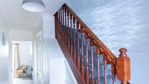 Una escalera con balaustres de madera y una alfombra azul, que conduce a una habitación con techo blanco y un marco de cuadro en la pared.