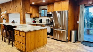 A modern kitchen with wooden cabinets, stainless steel appliances, and a large island with bar stools. - Lazy Bear Bungalow Pet Friendly Lake Escape  (Truckee)
