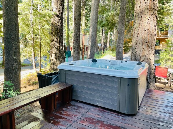 Un jacuzzi en una terraza de madera rodeado de árboles.