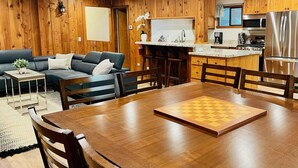 A cozy living room with a wooden wall, a sofa, a coffee table, and a chessboard on a wooden table. - Lazy Bear Bungalow Pet Friendly Lake Escape  (Truckee)