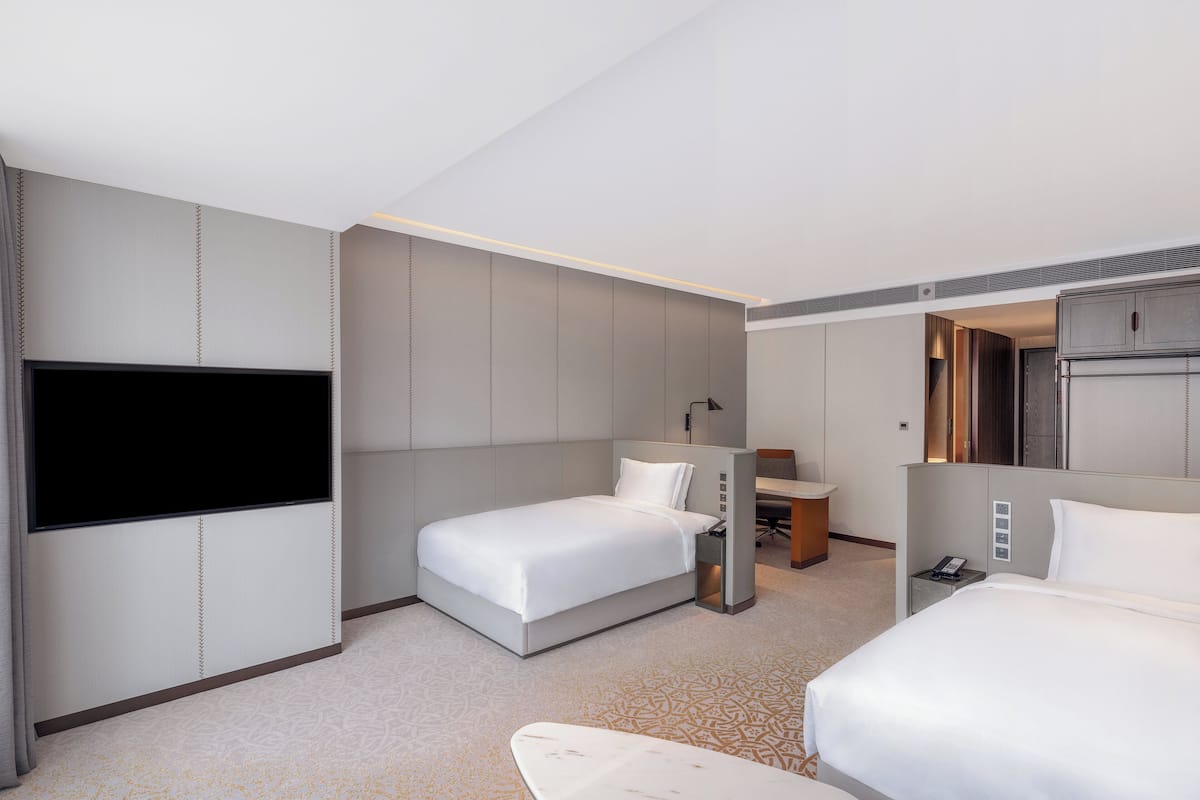 Ein Hotelzimmer mit großem Flachbildfernseher, zwei Betten, einem Schreibtisch und einer Minibar.