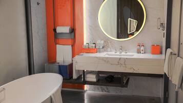 Un baño moderno con lavamanos de mármol, un espejo grande con luz circular y una bañera independiente.