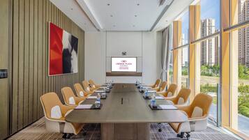 Une salle de conférence dotée d’une longue table, de nombreuses chaises, d’un grand écran et offrant une vue sur les bâtiments grâce à de grandes fenêtres.