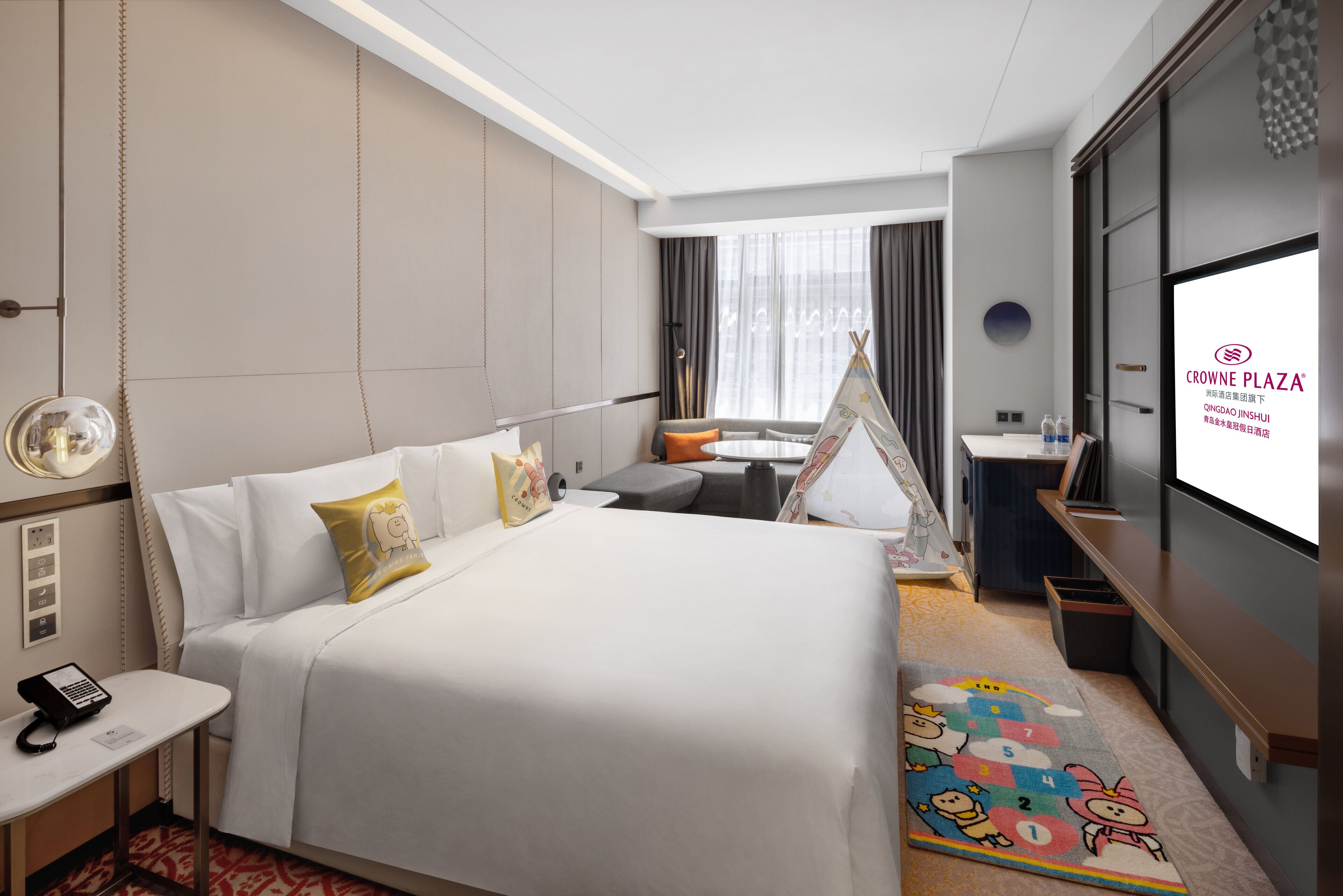 A hotel room with a large bed, a desk, a chair, a small table, a TV, and a wall-mounted shelf.
