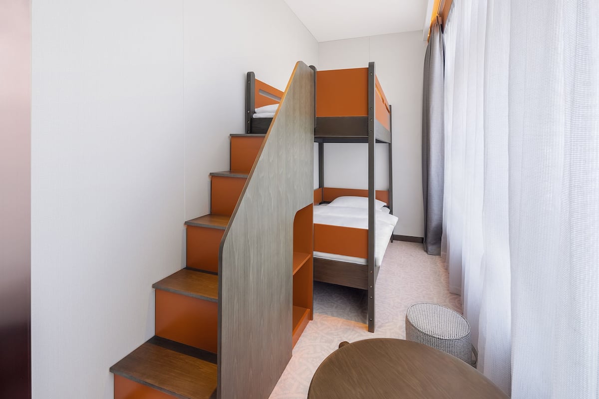 Ein kleines Zimmer mit einem Stockbett, einem kleinen runden Tisch und einem Korbstuhl.