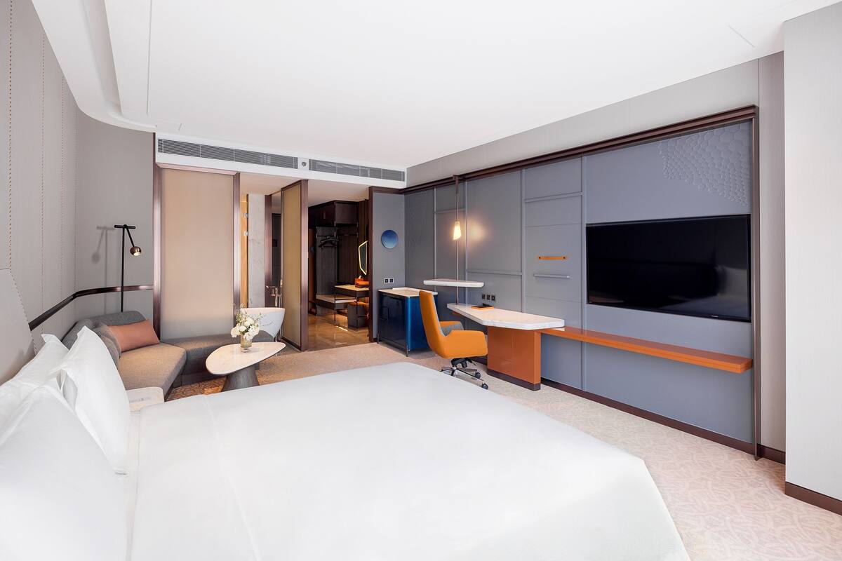 Ein modernes Hotelzimmer mit einem großen Bett, einem Schreibtisch mit Stuhl, einem Fernseher und einem begehbaren Kleiderschrank.