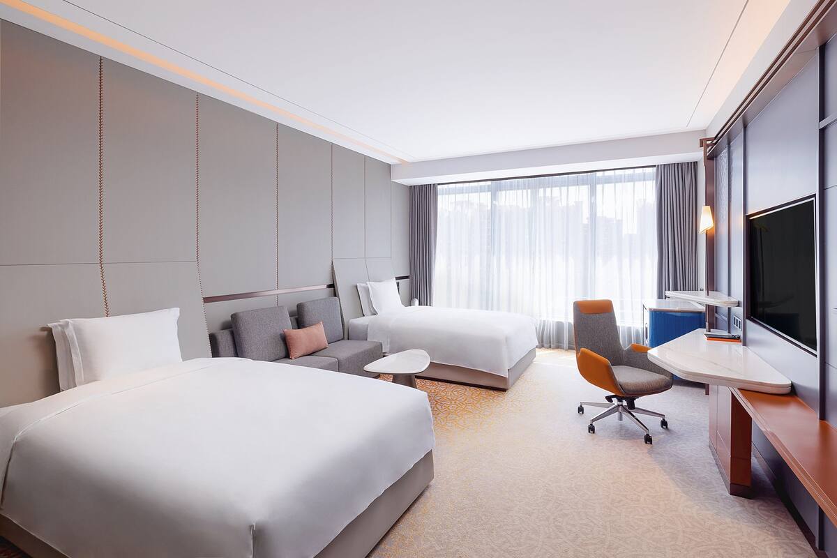 Ein Hotelzimmer mit zwei Betten, einem Sofa, einem Schreibtisch und einem Fernseher.