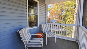 A porch with two chairs and a small table, a ceiling fan, and a view of trees and a house through a window. - Large Luxury 4 bed/3 bath Beach House-2 Blocks to beach, 1 Block to Bay (Colonial Beach)