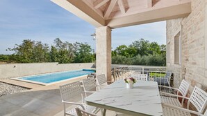 A covered outdoor area with a pool, white outdoor furniture, and stone walls.
