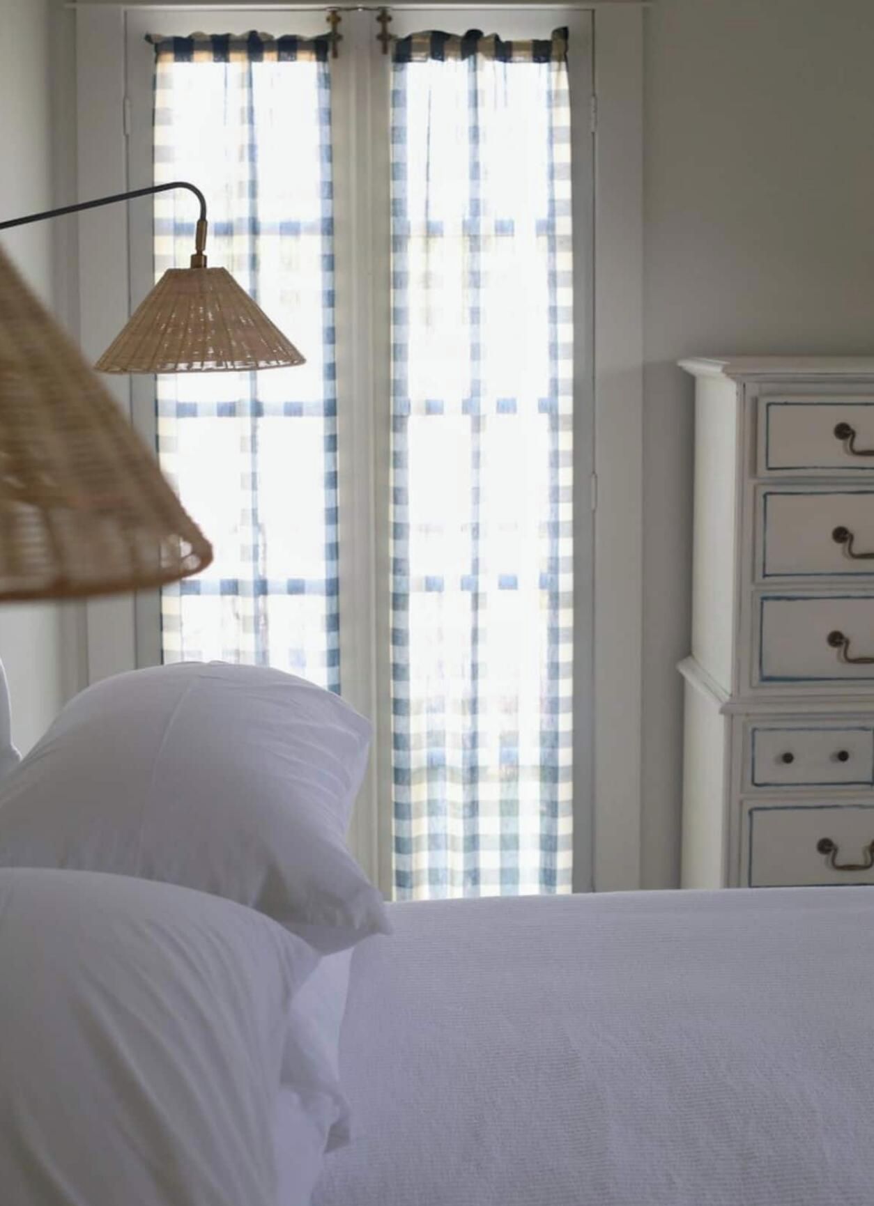 Une chambre à coucher avec un lit, une lampe suspendue et une fenêtre ornée de rideaux à carreaux.