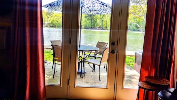 Een kamer met een schuifdeur naar een terras buiten, met een tafel en stoelen, een klein rond tafeltje en een decoratieve parasol.