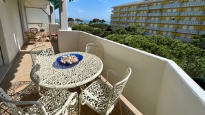 Ein Balkon mit rundem Tisch und weißen Stühlen, mit Blick auf ein Gebäude und Grünflächen.