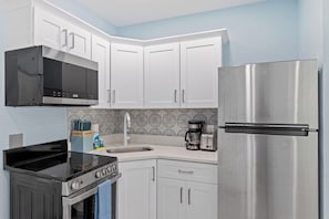 A kitchen with white cabinets, a black stove, a stainless steel refrigerator, and a microwave.