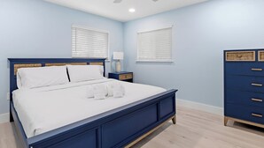A bedroom with a bed, nightstands, a dresser, a ceiling fan, and two windows with blinds.