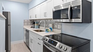 A modern kitchen with stainless steel appliances, white cabinetry, and patterned backsplash.