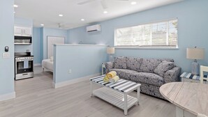 Ein modernes Wohnzimmer mit einer Couch, einem Couchtisch, einem Deckenventilator und einer Küchenzeile mit Backofen und Schränken.