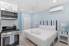 A hotel room with a bed, a nightstand, a wall-mounted air conditioner, a ceiling fan, and a built-in oven.