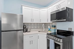 Una cocina con armarios blancos, un refrigerador de acero inoxidable, un microondas, una estufa y una cafetera.