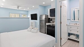 Ein Schlafzimmer mit Bett, Fernseher, Kühlschrank und einem Badezimmer mit Spiegel.