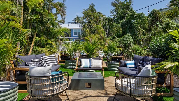 An outdoor seating area with wicker chairs and a central table, surrounded by lush greenery and palm trees. - The Hideaway Cottage at Palmview of Sanibel | Bikes | Beach gear (Sanibel)