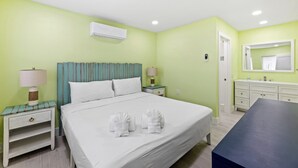 A hotel room with a bed, bedside tables, a desk, a mirror, and an air conditioning unit. - The Hideaway Cottage at Palmview of Sanibel | Bikes | Beach gear (Sanibel)