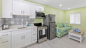 A compact kitchen with white cabinets, a stainless steel refrigerator, a built-in oven, and a microwave. - The Hideaway Cottage at Palmview of Sanibel | Bikes | Beach gear (Sanibel)
