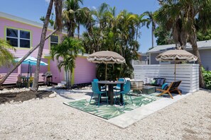 A patio with a table and chairs, surrounded by palm trees and a colorful building. - The Seagull Residence at The Sandpiper Inn of Sanibel | Bikes | Beach gear (Sanibel)