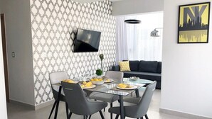 Ein moderner Essbereich mit einem Glastisch, grauen Stühlen und einem an der Wand befestigten Flachbildfernseher.
