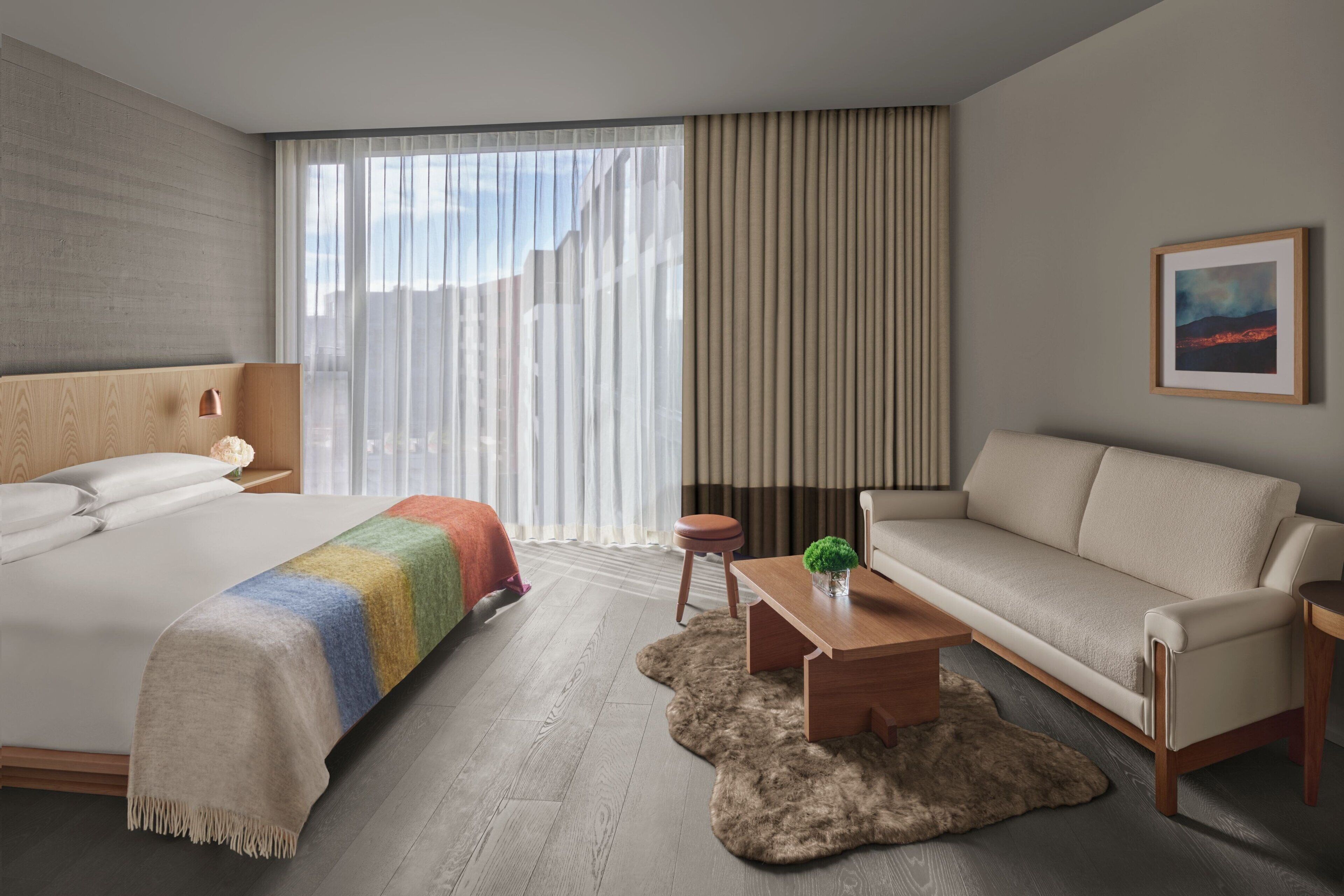 Een moderne hotelkamer met een groot bed, een bank, een klein tafeltje en een raam met gordijnen.