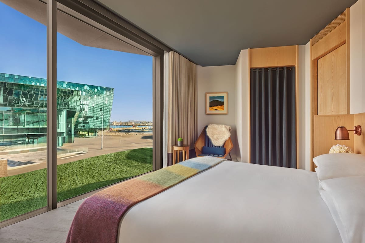 A hotel room with a large window, a bed, a chair, and a painting on the wall.