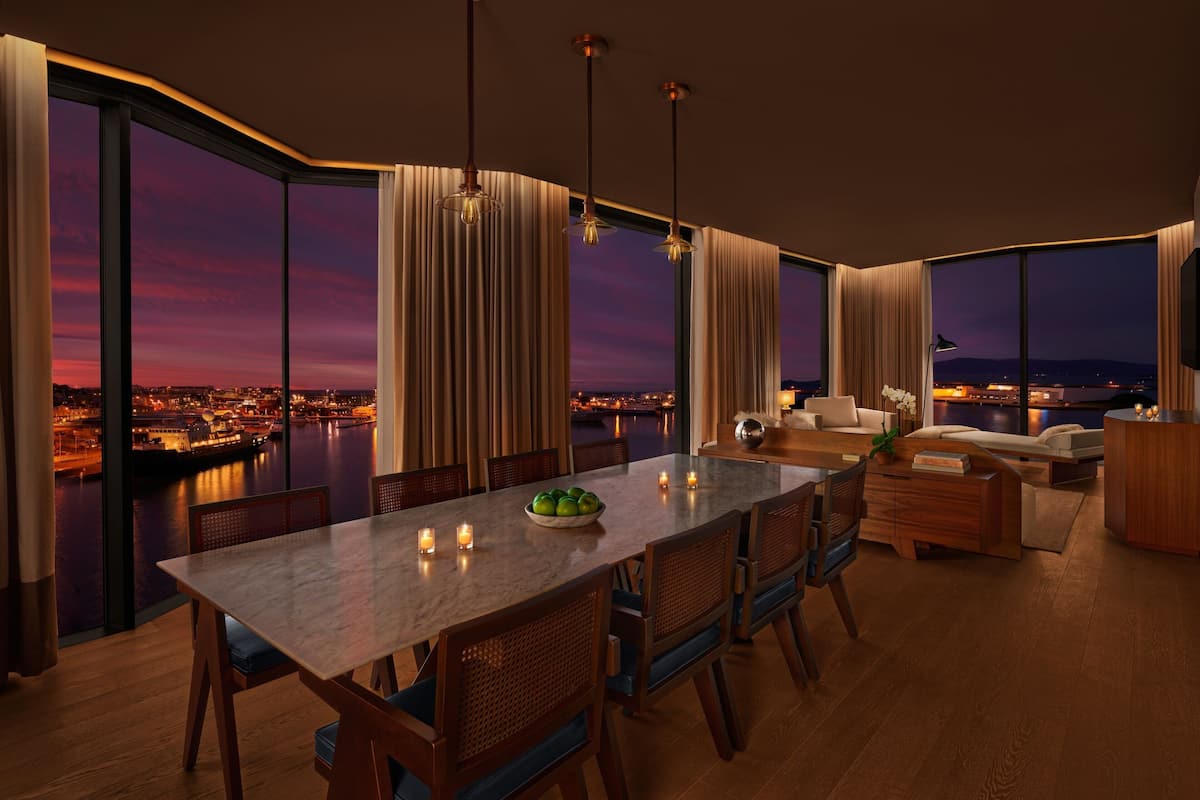 A modern dining area with a large table and chairs, a view of a cityscape at dusk, and a cozy seating area with a sofa and a coffee table.